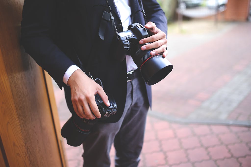 Close-up of a photographer holding DSLR cameras during a photo shoot outdoors.